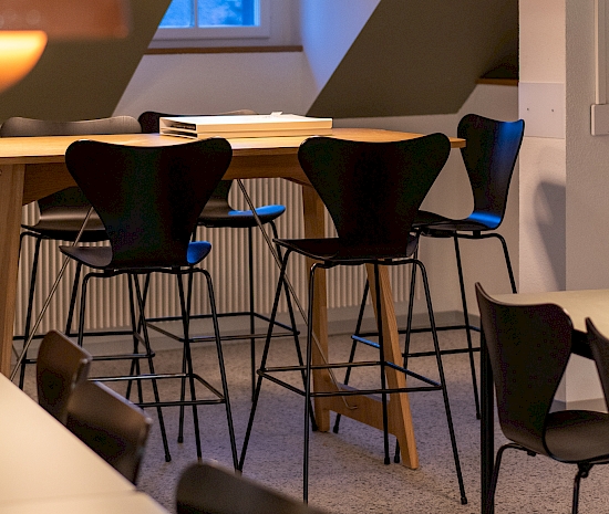 Kantine Loeb: Tische Alpha von Embru Spezialanfertigungen mit schwarzer Kante und schwarzem Untergestell, Stühle und Barhocker ohne Armlehne aus der Serie 7 von Fritz Hansen, Stehtische Desk von Vifian in Eiche, Lampen von &tradition, Modell Flowerpot VP7 und VP1
